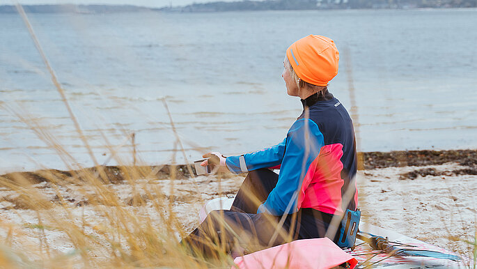 Eine Frau sitzt am Strand und blickt auf die Ostsee