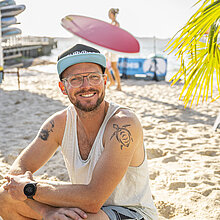 Ein Mann sitzt am Strand in Glücksburg an der Ostsee und lächelt in die Kamera