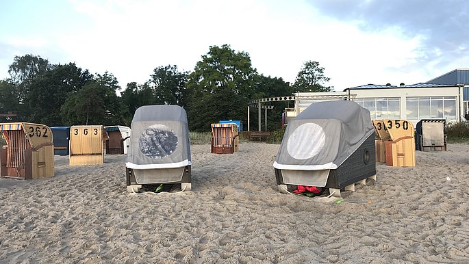 Zwei Schlafstrandkörbe stehen am Strand von Eckernförder. Im Hintergrund sind Strandkörbe zu sehen.