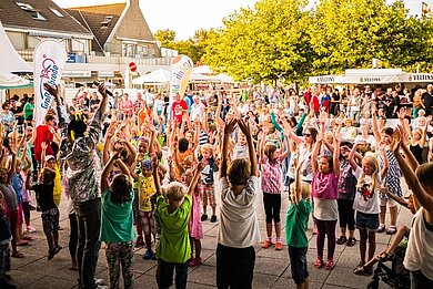 Viele Kinder, die alle die Hände in die Lüfte werfen und tanzen. 
