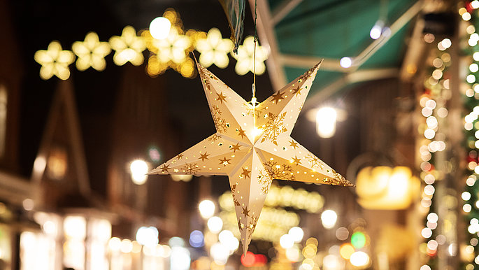 Ein glitzerner Stern in Nachaufnahme an einem geschmückten Tannenbaum auf einem Weihnachtsmarkt in der Holsteinischen Schweiz. 