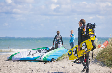 Personen sind mit Wassersport-Utensilien am Strand.