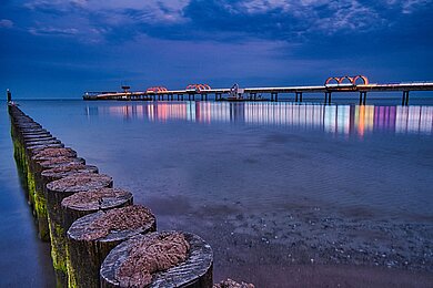 Die Seebrücke in Kellenhusen leuchtet in bunten Farben bei Nacht. 