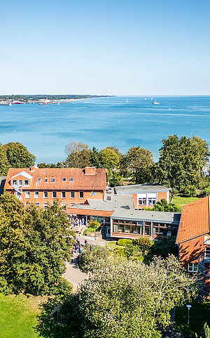 Luftbild vom Außengeländer der Jugendherberge in Eckernförde. Sie liegt direkt am Wasser mit Blick auf das Meer, und  umgeben von viel grünen Flächen. 