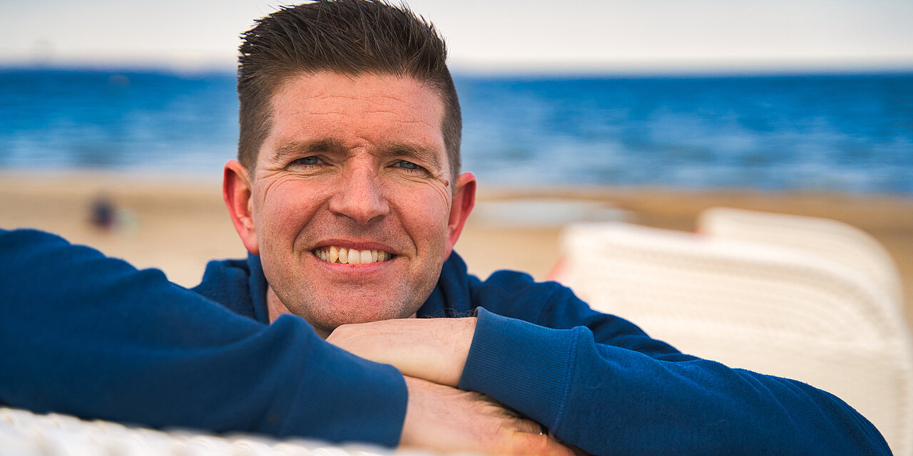 Portrait eines Mannes, der seine Hände auf seinem Strandkorb ablegt
