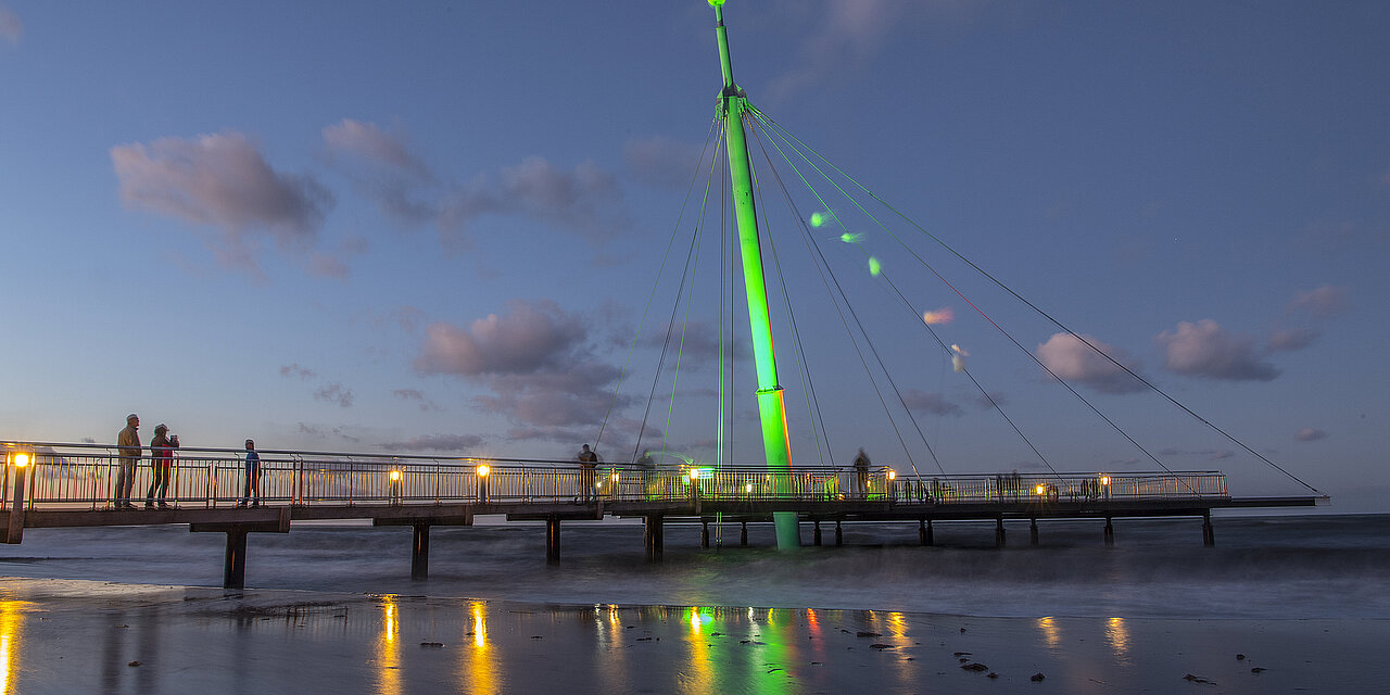 Lichtermeer in Hohwacht. Zu sehen ist die Seebrücke, sie wird von grünen Licht angestrahlt. Die Ostsee spiegelt die Lichtreflextionen.