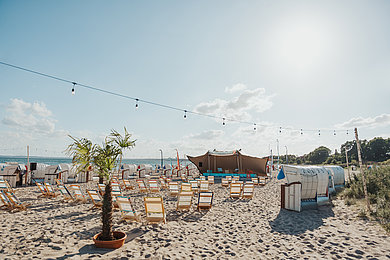 Am Strand ist eine Leinwand aufgebaut und viele Stühle stehen am Strand im Sand.