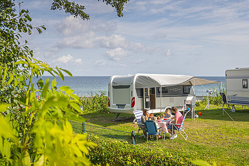 Eine Familie steht mit ihrem Wohnmobil auf dem Campingplatz in Surendorf bei Schwedeneck. Das Wetter ist sommerlich, sie haben Tisch und Stühle vor den weißen Wohnwagen plaziert.