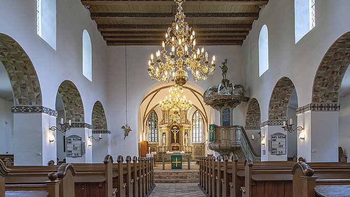 Eine Kirche von innen mit leuchtendem Kronleuchter über dem Mittelgang. 