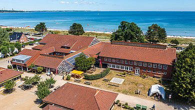 Luftbildaufnahme von der Jugendherberge Scharbeutz an einem sinnigen Tag. Auf dem Bild ist die Außenanlage der Jugendherberge und die direkte Nähe zur Ostsee zu sehen.