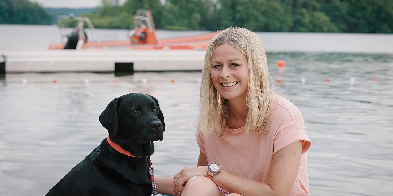 Eine Frau mit ihrem Hund sitzt auf ihrem SUP an einem See 