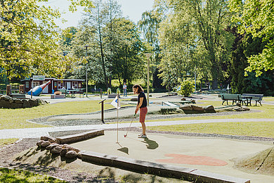 Eine Frau auf einer Mini-Golf-Anlage, steht mit dem Schläger in den Händen kurz vorm Schlag.