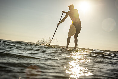 Mann steht auf dem SUP mitten auf der Ostsee.