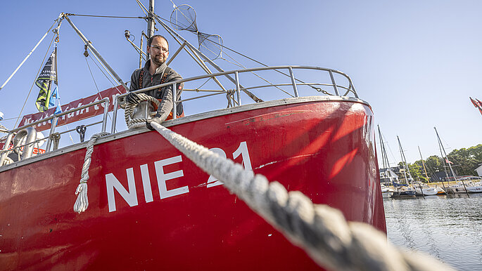 Peter steht auf seinem roten Fischerboot und zieht das Seil fest.