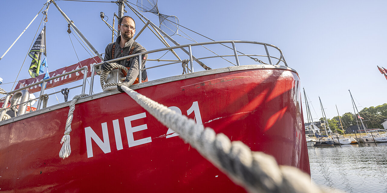 Peter steht auf seinem roten Fischerboot und zieht das Seil fest.