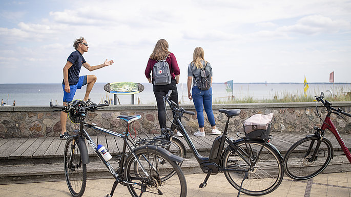 Radfahrer neben ihren Rädern blicken auf das Meer.