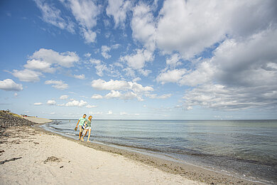 Ein fast menschenleerer Strand, ein paar helle Schäfchen-Wolken sind am Himmel