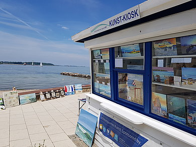Ein blau-weiß gestrichener Kiosk aus Holz steht an der Promenade direkt am Strand von Heikendorf. 