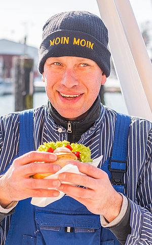 Ein Fischer mit Fischbrötchen in der Hand steht am Hafen