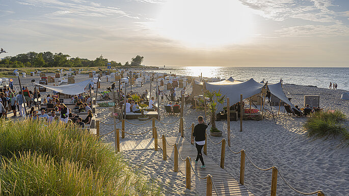 Strandbar in Heiligenhafen. Von der Promenade aus sieht man die Strandbar. Viele Gäste sitzen in der Strandbar und lassen den Abend ausklingen.