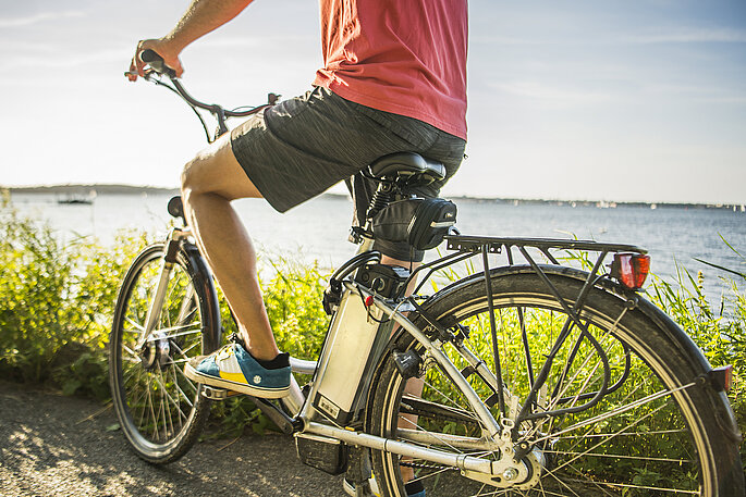 Mann sitzt auf einem E-Bike. Kurze Pause an der Steilküste der Kieler Förde mit Blick auf die Ostsee.