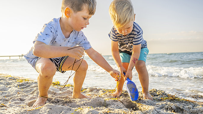 Zwei Kinder buddeln im Sand am Strand. 