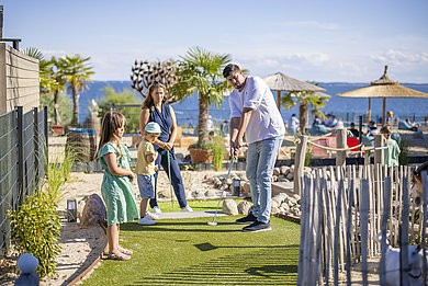 Eine Familie spielt Adventure Golf. Der Papa schlägt gerade den Ball mit seinem Schläger.