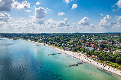 Luftaufnahme vom Hauptstrand in Eckernförde. Links auf dem Bild sieht man die Ostsee. Rechts den Strand und das Festland mit Häusern, und Bäumen.
