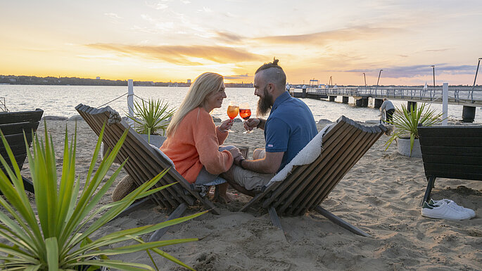 Pärchen sitzt in der Strandbar in Mönkeberg mit einem Cocktail in der Hand.