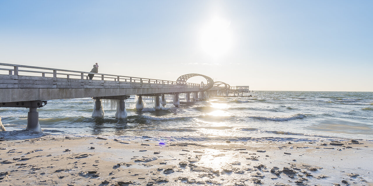 Eine Seebrücke mit ragt ins Meer, die Sonne geht auf. 