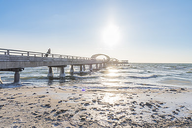 Eine Seebrücke mit ragt ins Meer, die Sonne geht auf. 