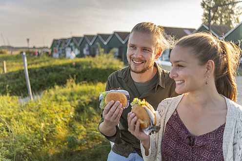 Zwei Leute gehen mit einem Fischbrötchen in der Hand in Hohwacht spazieren