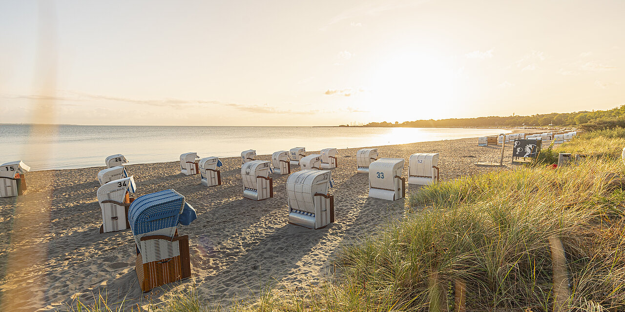 Die Sonne geht über der Ostsee unter, am Strand sind Strandkörbe aufgestellt.