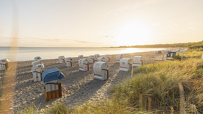 Die Sonne geht über der Ostsee unter, am Strand sind Strandkörbe aufgestellt.