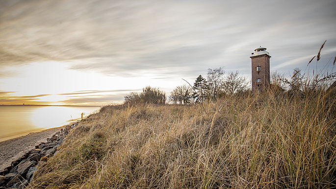 Sonnenuntergang an der Küste. Rechts im Bild viel Dünen, dahinter liegt der Leuchtturm von Pelzerhaken.