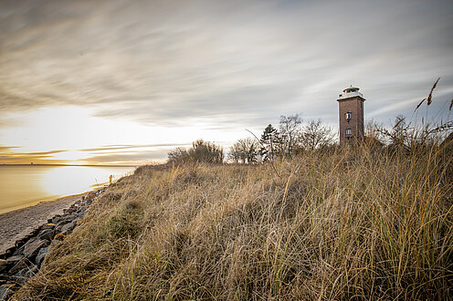 Sonnenuntergang an der Küste. Rechts im Bild viel Dünen, dahinter liegt der Leuchtturm von Pelzerhaken.