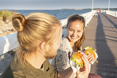 Zwei Frauen spazieren mit Fischbrötchen über die Seebrücke