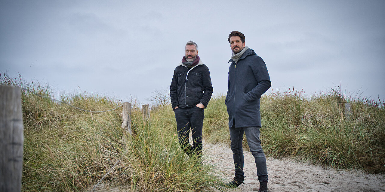 Zwei Männer stehen an den Dünen der Ostsee