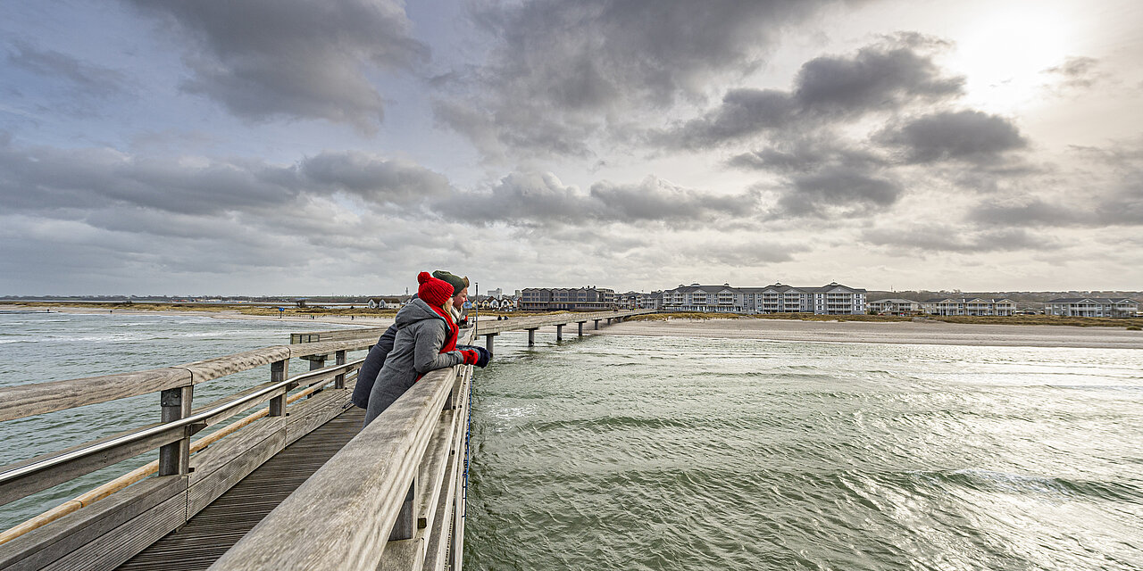 Zwei Personen stehen auf der Seebrücke und blicken auf die Ostsee.