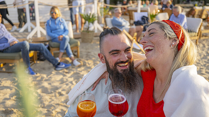 Paar am Strand mit Getränken in die Hand und am lachen