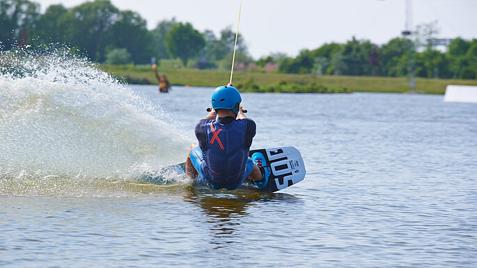 Wakeboarder von hinten. Das Wasser spritzt. 