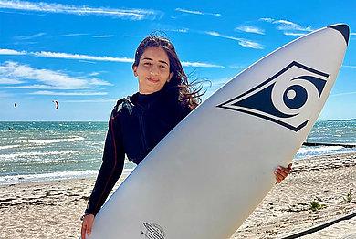 eine Frau mit einem SUP in den Händen am Strand. 