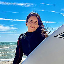 eine Frau mit einem SUP in den Händen am Strand. 