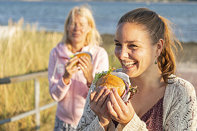 Zwei Frauen essen Fischbröchten am Strand in Hohwacht.