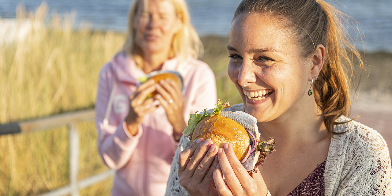 Zwei Frauen essen Fischbröchten am Strand in Hohwacht.