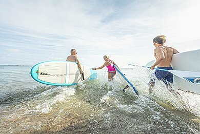 Eine Gruppe von Menschen mit SUP Boards unter dem Arm rennen ins Meer