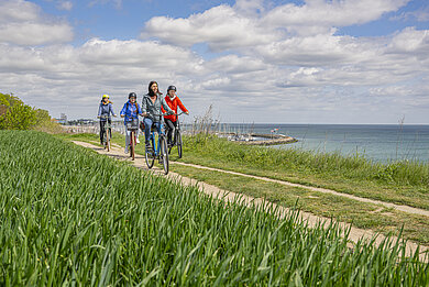 Vier Personen radeln auf der Steilküste. Recht siehst du die Ostsee.