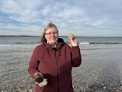 Eine Frau am Strand von Eckernförde. Sie hält einen Stein in die Kamera und lächelt. 