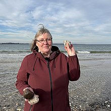 Eine Frau am Strand von Eckernförde. Sie hält einen Stein in die Kamera und lächelt. 