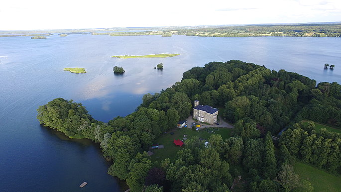 Eine Luftaufnahme vom Schloss Ascheberg. Esliegt direkt am See und ist umgeben von Grün. 